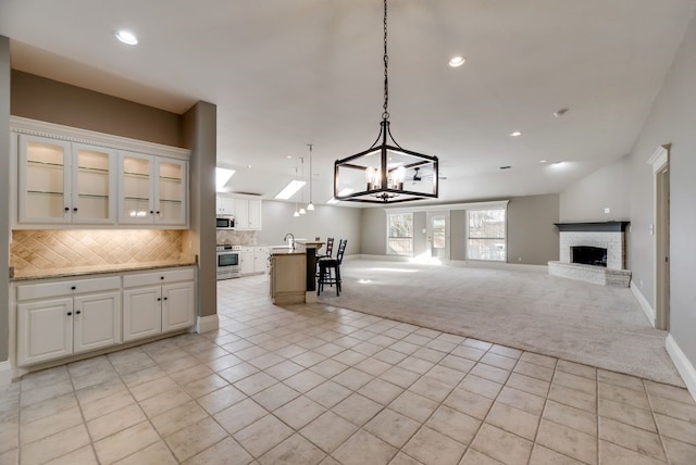 kitchen with a kitchen island with sink, decorative backsplash, decorative light fixtures, stainless steel range oven, and white cabinetry