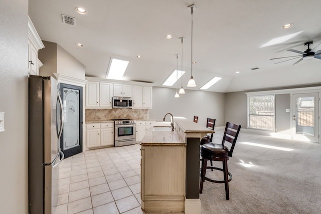 kitchen featuring lofted ceiling with skylight, sink, hanging light fixtures, light stone counters, and stainless steel appliances