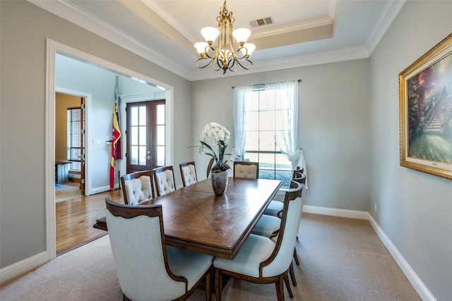 dining room featuring french doors, crown molding, a tray ceiling, a notable chandelier, and light colored carpet