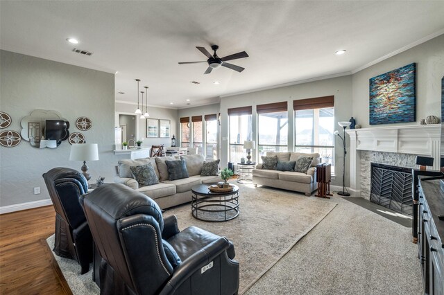 living room with hardwood / wood-style floors, a stone fireplace, ceiling fan, and ornamental molding