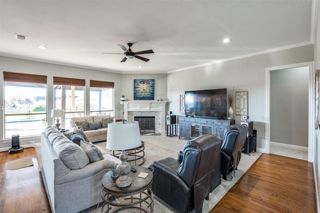 living room featuring a premium fireplace, hardwood / wood-style floors, ceiling fan, and crown molding