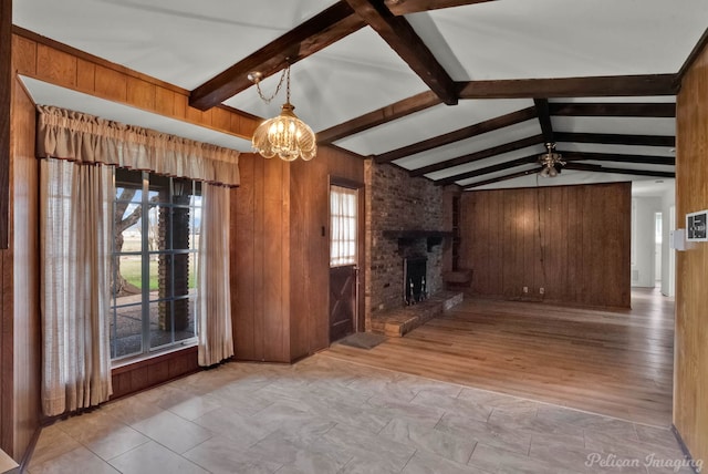 unfurnished living room with a fireplace, ceiling fan with notable chandelier, wooden walls, and lofted ceiling with beams