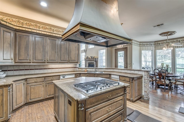 kitchen with custom exhaust hood, sink, a kitchen island, kitchen peninsula, and stainless steel gas cooktop