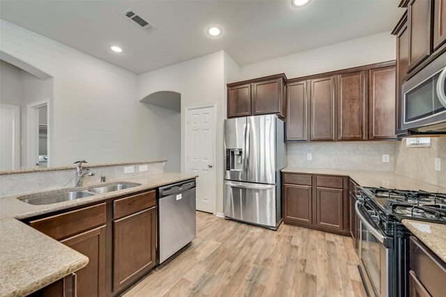 kitchen featuring sink, tasteful backsplash, light stone counters, light hardwood / wood-style floors, and appliances with stainless steel finishes