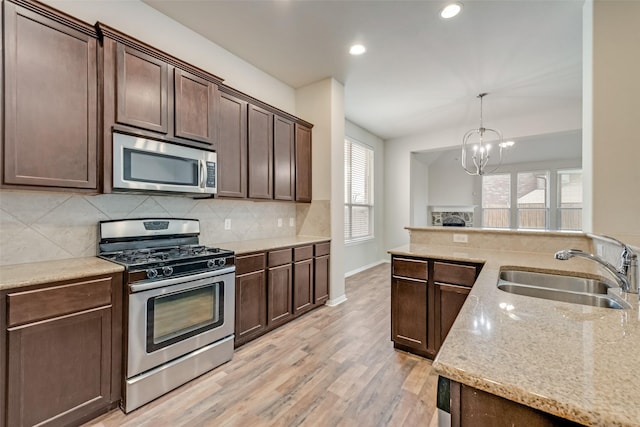 kitchen with dark brown cabinets, stainless steel appliances, sink, light hardwood / wood-style flooring, and a notable chandelier