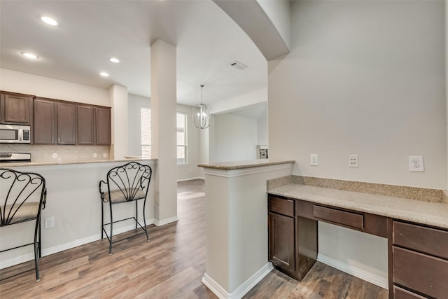 kitchen featuring dark brown cabinetry, a notable chandelier, kitchen peninsula, pendant lighting, and a breakfast bar