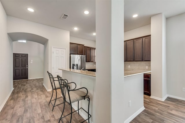 kitchen featuring stainless steel refrigerator with ice dispenser, light hardwood / wood-style flooring, tasteful backsplash, dark brown cabinetry, and a breakfast bar area