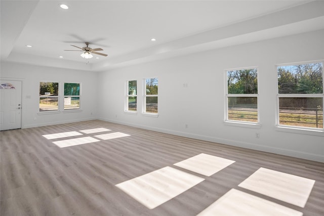 unfurnished living room with a raised ceiling, ceiling fan, a healthy amount of sunlight, and light hardwood / wood-style floors