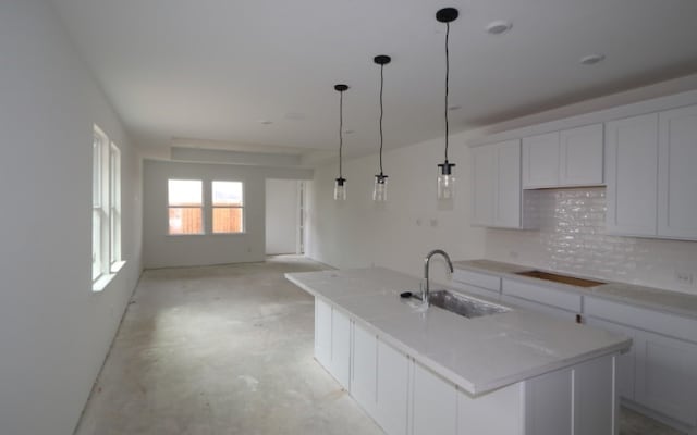 kitchen featuring a kitchen island with sink, sink, stovetop, white cabinetry, and hanging light fixtures