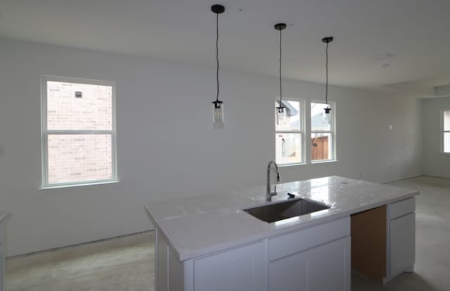 kitchen featuring light stone countertops, sink, white cabinets, hanging light fixtures, and an island with sink