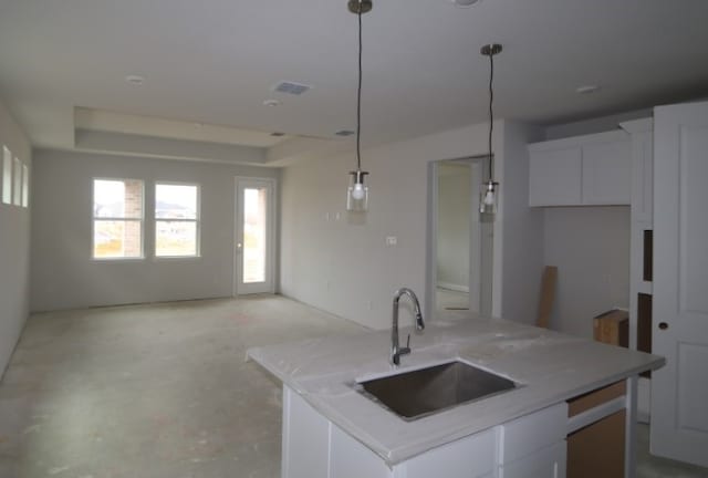 kitchen featuring sink, a raised ceiling, an island with sink, pendant lighting, and white cabinets