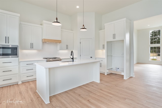 kitchen featuring black microwave, a kitchen island with sink, white cabinets, and decorative light fixtures