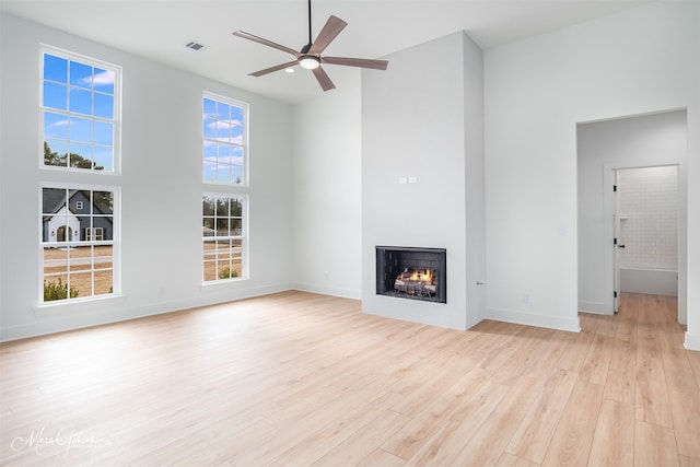 unfurnished living room with ceiling fan, a towering ceiling, and light wood-type flooring