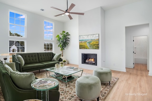 living room with a towering ceiling, ceiling fan, and light wood-type flooring