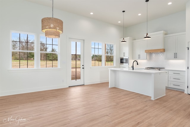 kitchen featuring pendant lighting, stainless steel microwave, a center island with sink, and white cabinets