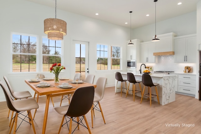 dining room featuring a towering ceiling, sink, and light hardwood / wood-style flooring