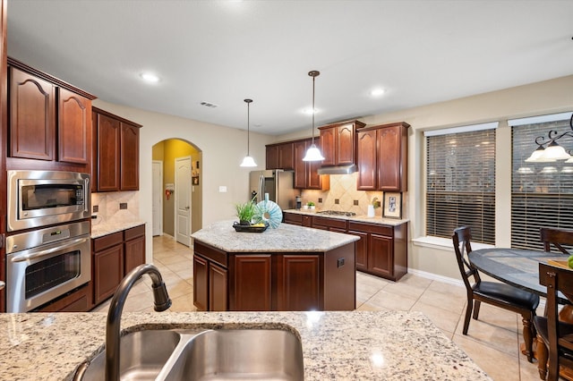 kitchen with stainless steel appliances, backsplash, hanging light fixtures, a kitchen island, and sink