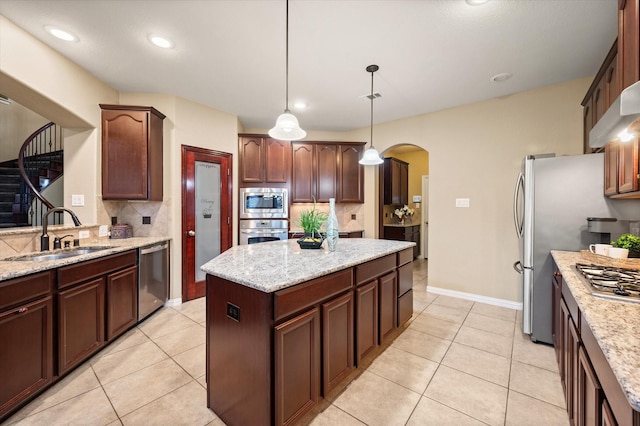 kitchen with light stone countertops, appliances with stainless steel finishes, decorative light fixtures, tasteful backsplash, and sink