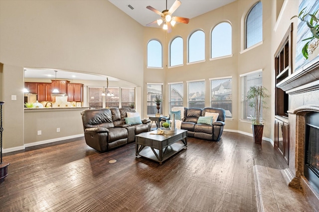 living room featuring dark wood-type flooring, ceiling fan with notable chandelier, a high ceiling, and a tile fireplace