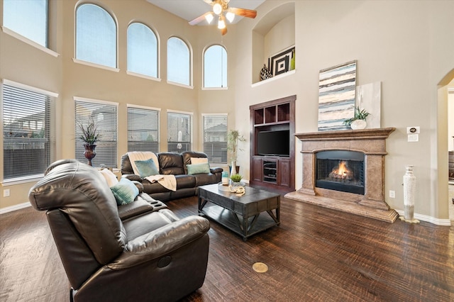 living room featuring dark wood-type flooring, a high end fireplace, a high ceiling, and built in shelves