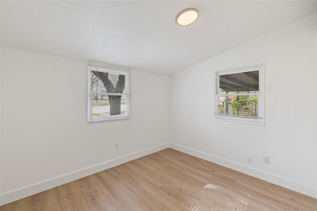 empty room featuring plenty of natural light, light hardwood / wood-style floors, and lofted ceiling