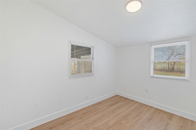 unfurnished room with a healthy amount of sunlight, vaulted ceiling, and light hardwood / wood-style floors