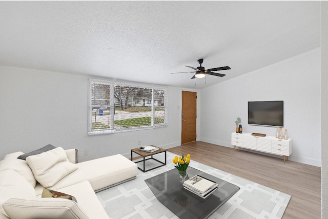 living room with a textured ceiling, light wood-type flooring, and ceiling fan