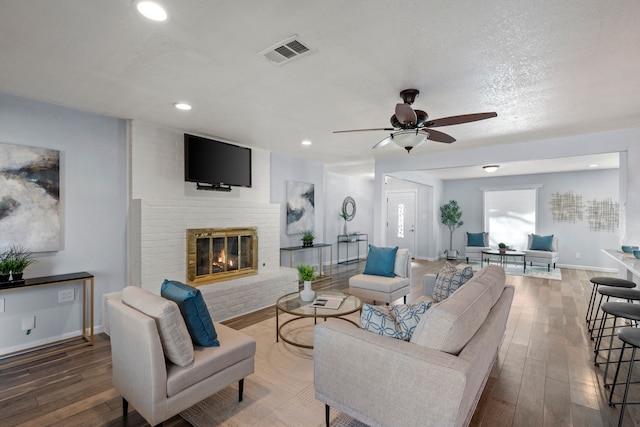 living room with a brick fireplace, hardwood / wood-style floors, a textured ceiling, and ceiling fan