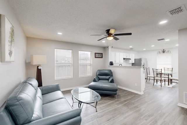 living room with ceiling fan, a textured ceiling, and light wood-type flooring