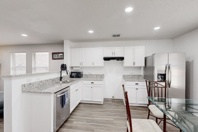 kitchen with sink, appliances with stainless steel finishes, white cabinetry, light stone countertops, and kitchen peninsula