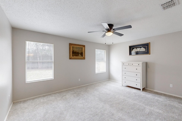 unfurnished bedroom featuring multiple windows, ceiling fan, light colored carpet, and a textured ceiling