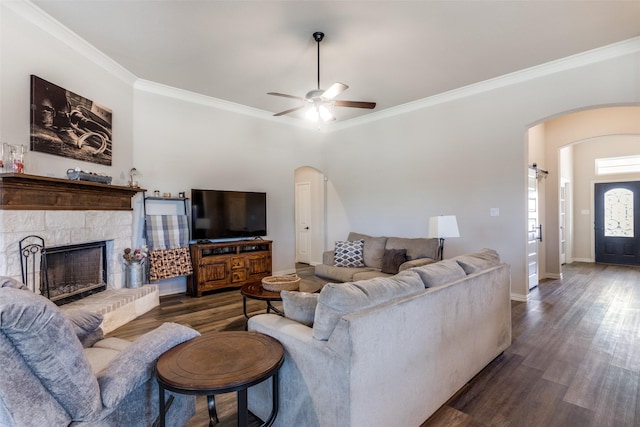 living room featuring a stone fireplace, ceiling fan, dark hardwood / wood-style flooring, and ornamental molding