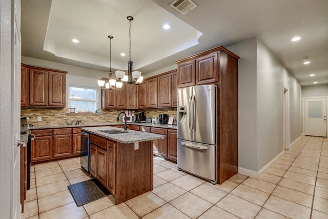 kitchen with sink, stainless steel appliances, backsplash, an island with sink, and a tray ceiling