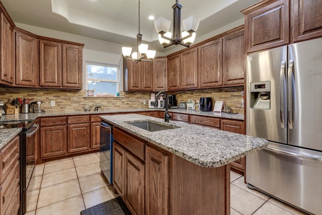 kitchen featuring hanging light fixtures, light tile patterned floors, a tray ceiling, stainless steel appliances, and a kitchen island with sink