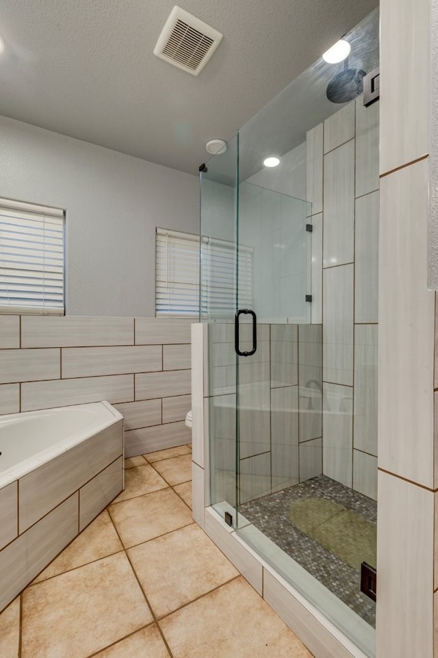 bathroom featuring shower with separate bathtub, tile walls, toilet, tile patterned floors, and a textured ceiling