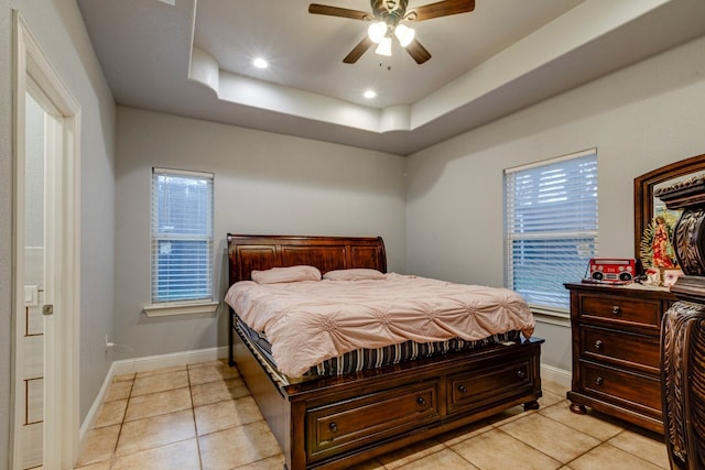 bedroom with ceiling fan, a tray ceiling, multiple windows, and light tile patterned floors