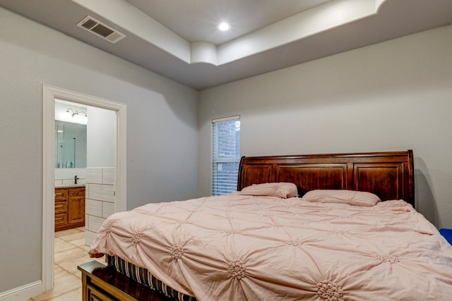 bedroom featuring ensuite bathroom, a tray ceiling, and light tile patterned floors