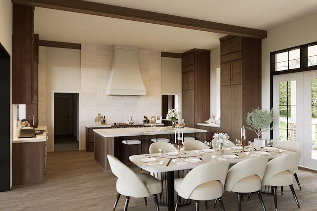 kitchen with beam ceiling, light wood-type flooring, a towering ceiling, and premium range hood