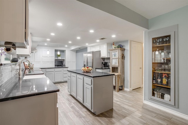 kitchen with stainless steel fridge with ice dispenser, a center island, white cabinetry, and sink