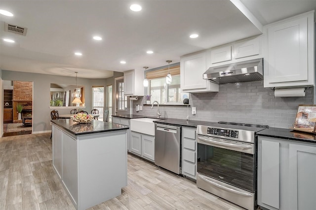 kitchen featuring appliances with stainless steel finishes, sink, white cabinetry, hanging light fixtures, and range hood