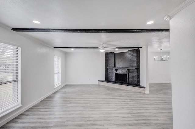 unfurnished living room with a brick fireplace, crown molding, a textured ceiling, ceiling fan with notable chandelier, and light wood-type flooring