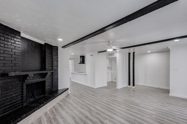 unfurnished living room with light hardwood / wood-style flooring, ceiling fan, a textured ceiling, a brick fireplace, and beamed ceiling