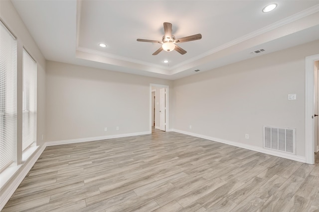 empty room featuring ceiling fan, ornamental molding, a tray ceiling, and light wood-type flooring