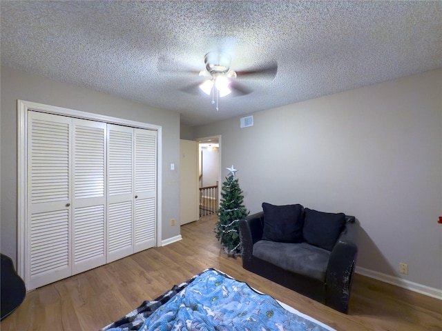 bedroom featuring a textured ceiling, ceiling fan, wood finished floors, visible vents, and a closet