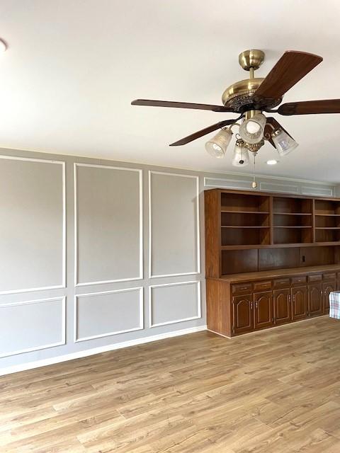 interior space with light wood finished floors, a ceiling fan, and a decorative wall