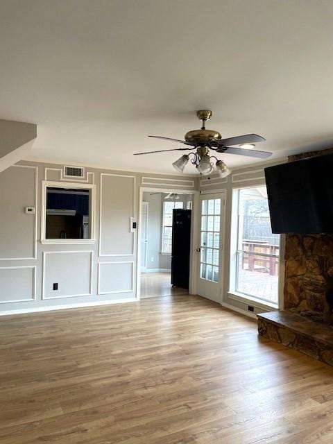 unfurnished living room with ceiling fan, light wood finished floors, visible vents, and a decorative wall