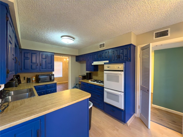 kitchen with blue cabinetry, kitchen peninsula, sink, and white appliances