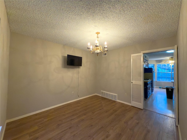 empty room with dark wood-style flooring, visible vents, a textured ceiling, a chandelier, and baseboards