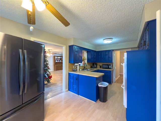 kitchen featuring blue cabinetry, light countertops, freestanding refrigerator, a sink, and a peninsula