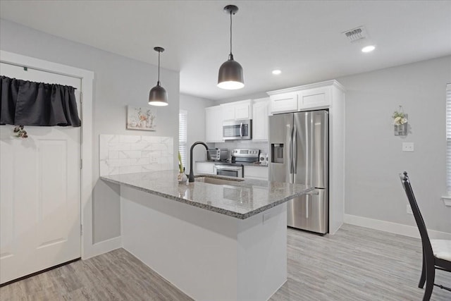 kitchen featuring pendant lighting, appliances with stainless steel finishes, white cabinetry, light stone countertops, and kitchen peninsula